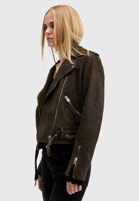 Giacca da motociclista in suede marrone con design aderente, chiusura a zip asimmetrica, tasche con zip e dettaglio in vita con cinturino.