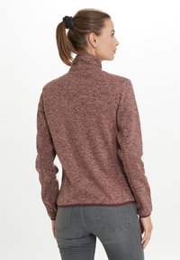 Fleecejacka i vinröd med ett texturerat mönster, hög krage och långa ärmar. Bärs med grå jeans, har en smal passform och slät finish.