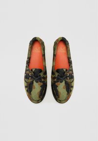 Grønne og sorte camo-mønstrede loafers med en pelsagtig tekstur, med orange indersåler og sorte snørebånd, samt en rund tådesign.