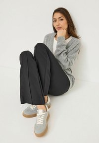 Un cardigan gris en tricot porté sur un top blanc, associé à un pantalon noir taille haute et des baskets grises avec des accents beiges et des semelles en caoutchouc.