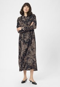 Rochie lungă, cu guler, de culoare neagră, cu un model abstract maro. Cu mâneci lungi, croi lejer, care se termină sub genunchi. Asortată cu mule cu toc negre.
