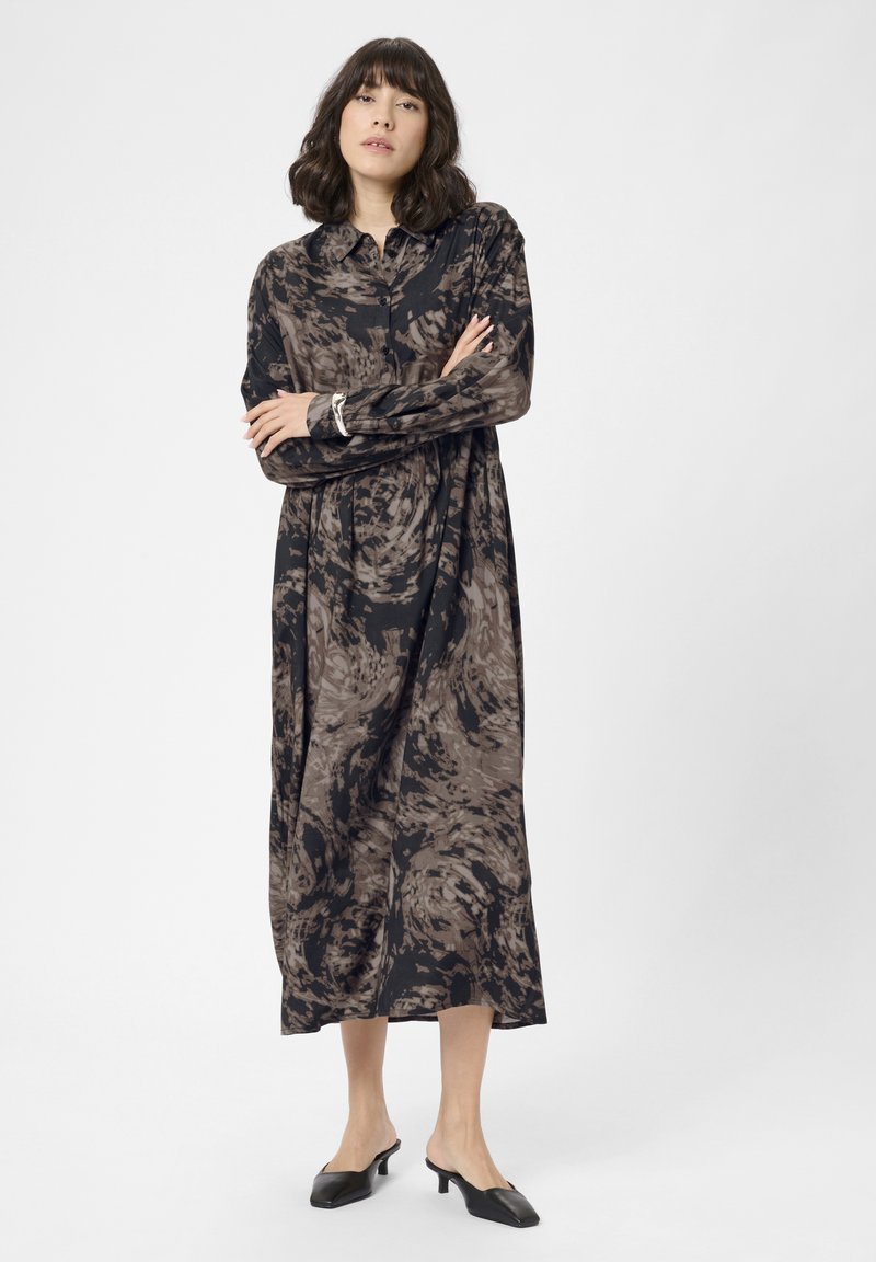 Rochie lungă, cu guler, de culoare neagră, cu un model abstract maro. Cu mâneci lungi, croi lejer, care se termină sub genunchi. Asortată cu mule cu toc negre.