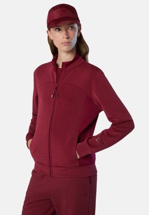 Giacca con zip color bordeaux, colletto alto, maniche lunghe e tasche laterali. Texture liscia; piccolo logo sul maniche.