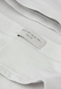 Ljust grått tyg med en slät struktur och subtil lyster. Har en etikett med texten "Intimissimi Natura." Sömmen är prydlig och konsekvent.