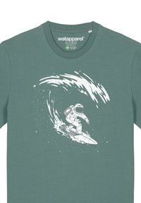 T-shirt en coton teal avec un graphique blanc représentant un astronaute surfant sur une vague, entouré de particules ressemblant à des étoiles et de lignes de mouvement dynamiques.