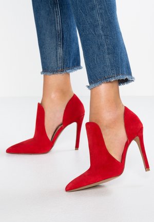 Red suede high-heeled shoes with a pointed toe and side cutouts. The design features a sleek stiletto heel and a smooth texture.