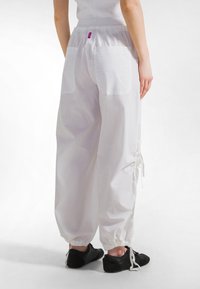 Hvide, løstsiddende bomuldsbukser med elastisk talje og to påsyede lommer. Justerbar snøre ved fodenden. Blød tekstur.