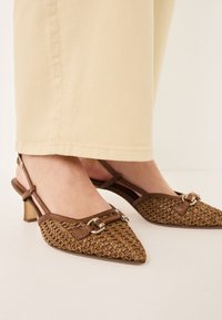 Tacchi slingback intrecciati marroni con punta appuntita e una fibbia decorativa in metallo. Tomaia testurizzata con tacco basso a blocco.