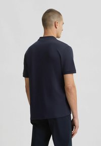 Polo de manga corta azul marino oscuro hecho de algodón, con un cuello con costuras decorativas y un dobladillo recto.