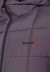 Kurtka pikowana w ciemnofioletowym materiale z pikowanym wzorem. Posiada czarny zamek błyskawiczny i haftowane czerwone logo.