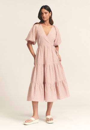 Pink gingham wrap dress with short puff sleeves, tiered skirt, and side tie. Worn with white platform sandals. Smooth cotton fabric.