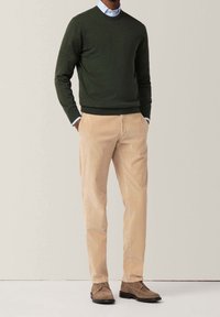 Maglione in cotone verde scuro, camicia colletto azzurro chiaro sotto, chinos beige e scarpe in suede marroni, slim fit con design semplice.