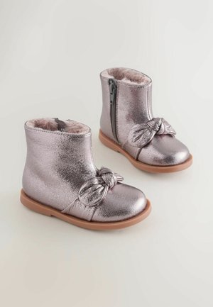 Bottes de cheville métalliques roses avec doublure en fourrure et fermeture éclair sur le côté. Présente un accent de nœud noué à l'avant et une semelle en caoutchouc brun.
