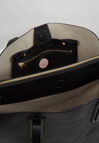 Sort læder tote bag med en tekstureret overflade, der har en guldfarvet lynlås, beige indvendig foret og en lille indvendig lynlåslomme.