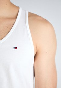 Weißes Baumwoll-Tanktop mit Rundhalsausschnitt. Verfügt über ein kleines gesticktes Logo in Marineblau, Rot und Weiß auf der linken Brustseite.