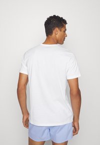 White cotton t-shirt with short sleeves, round neckline, and a straight hem. Worn with blue checkered shorts. Plain design, no patterns.