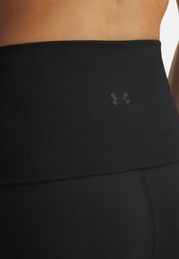 Cinturilla atlética negra de cintura alta con tejido acanalado, textura suave y un logo sutil, conectada a leggings negros ajustados.