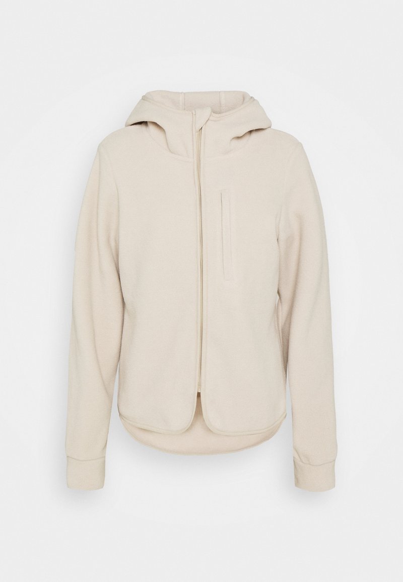 Sweat à capuche beige zippé avec une poche avant, une capuche et des poignets et ourlet côtelés. Texture douce et tissu lisse avec un ourlet inférieur arrondi.