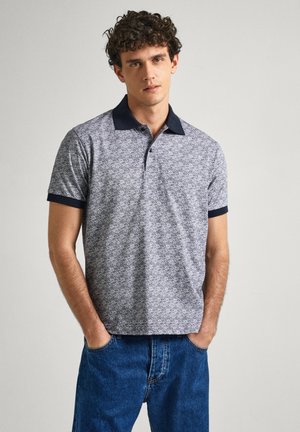Navy and gray patterned polo shirt with a solid navy collar and sleeves, made of cotton, featuring a casual fit. Dark denim jeans.