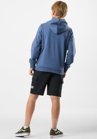 Felpa blu con tasca a marsupio, pantaloni cargo neri e sneakers verdi. La felpa presenta una vestibilità comoda e polsini a costine.