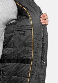 Szara kurtka puchowa z żółtym wykończeniem wewnętrznym. Posiada zamek błyskawiczny, kieszeń wewnętrzną oraz pikowany design dla lepszej izolacji.