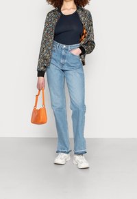 Giacca bomber floreale, top blu navy, jeans chiari a vita alta, borsa arancione e sneakers bianche con suole testurizzate.