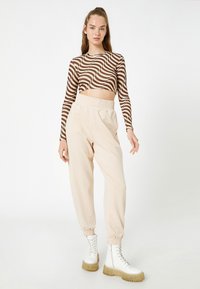 Długi rękaw crop top w brązowe faliste paski, w połączeniu z beżowymi spodniami dresowymi z elastyczną talią i elastycznymi mankietami. Białe buty wojskowe.