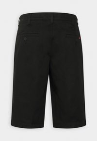 Short noir longueur genou avec passants pour ceinture, deux poches arrière boutonnées et une petite étiquette logo rouge sur la poche droite.