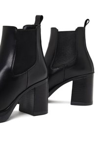 Botas de cuero negro hasta el tobillo con punta redonda, paneles laterales elásticos y un tacón alto y grueso. Textura suave con un grano sutil.