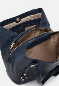 Tmavě modrá kožená kabelka s texturovaným povrchem, zlatými zipy, béžově podloženým interiérem a několika přihrádkami.