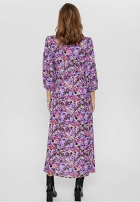 Fladdrande lila blommig klänning med puffärmar. Har en blandning av rosa, lila och bruna blommor på ett lätt tyg. Längden når till mitten av vaden.