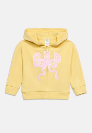 Κίτρινο φούτερ ζιπ-επί με κουκούλα για νήπια, με ροζ γράμματα "GAP" και διακοσμητικό ροζ φιόγκο στο μπροστινό μέρος.