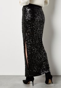 Schwarzer Paillettenrock mit taillierter Passform, seitlichen Schlitzen und glatter Textur, kombiniert mit schwarzen High Heels.