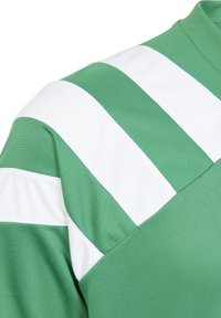 Tela verde con rayas diagonales blancas en el hombro y la parte superior del brazo, detalles de costura visibles en el textil suave.