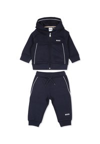 Ensemble de hoodie et pantalon bleu foncé en matériau doux. Présente des accents blancs, une fermeture zippée, et un logo sur les deux pièces. Convient pour un usage décontracté.