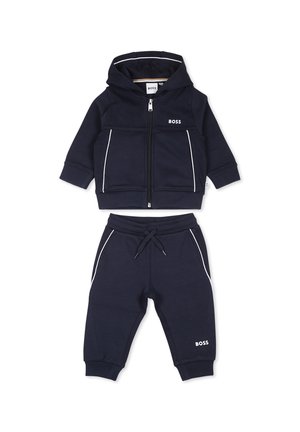 Ensemble de hoodie et pantalon bleu foncé en matériau doux. Présente des accents blancs, une fermeture zippée, et un logo sur les deux pièces. Convient pour un usage décontracté.