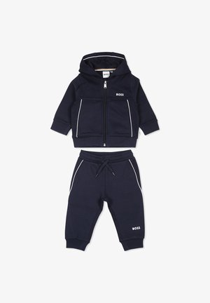 Set di felpa e pantaloni blu scuro realizzato in materiale morbido. Presenta dettagli bianchi, chiusura con zip e logo su entrambi i pezzi. Adatto per un abbigliamento casual.