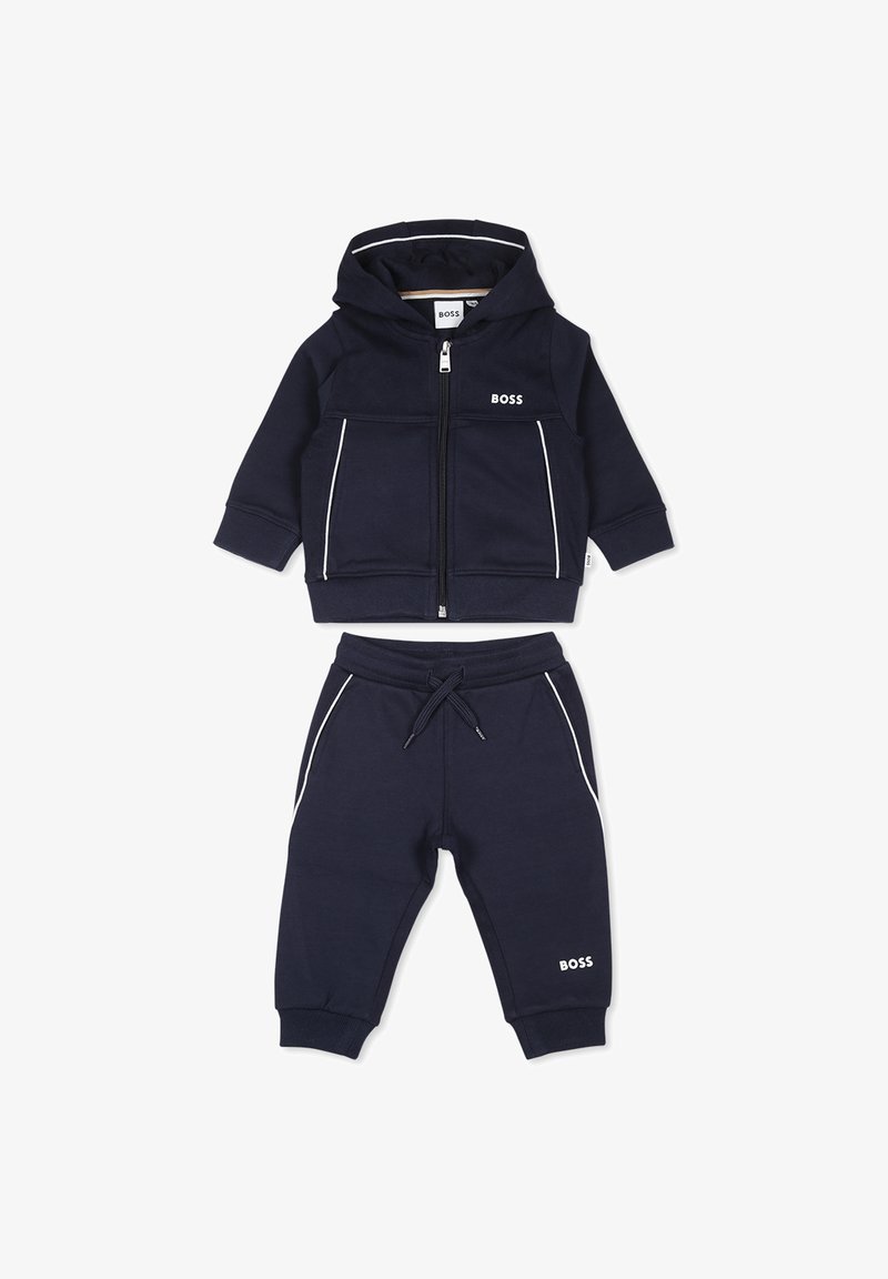 Ensemble de hoodie et pantalon bleu foncé en matériau doux. Présente des accents blancs, une fermeture zippée, et un logo sur les deux pièces. Convient pour un usage décontracté.