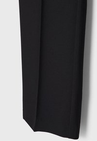 Jambe de pantalon noir sur mesure avec un pli marqué à l'avant, montrant une couture propre et une texture de tissu lisse.