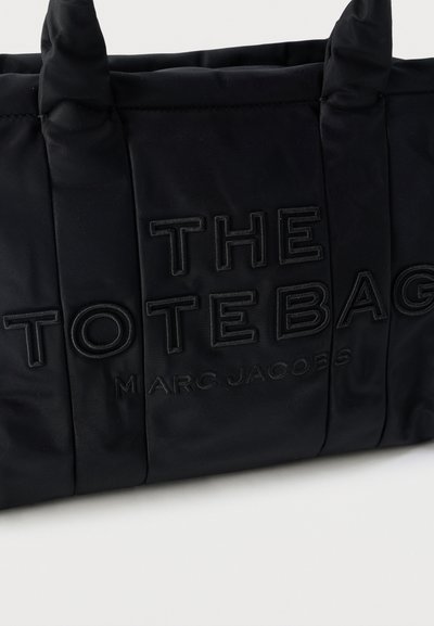 Μαύρη τσάντα tote Marc Jacobs με επενδεδυμένες λαβές και ανάγλυφο κείμενο "THE TOTE BAG" στην πρόσοψη.