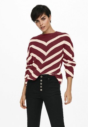 Maglione a righe rosse e crema con motivo a zigzag, texture lavorata a maglia, scollatura rotonda e maniche arrotolate, abbinato a jeans neri a vita alta.