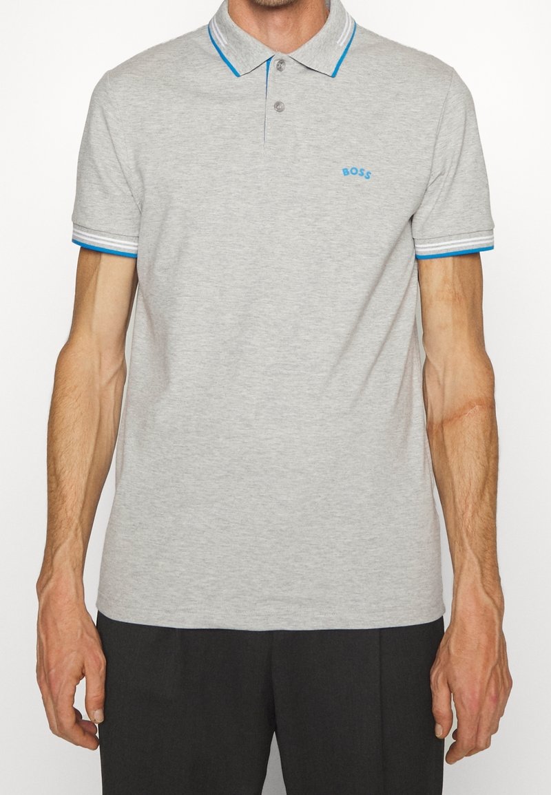 Polo gris avec un col classique, des poignets rayés bleus et blancs, arborant un petit logo bleu sur la poitrine. Matière douce en mélange de coton.