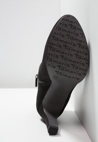 Czarne zamszowe botki za kostkę z ostro zakończonym noskiem, z zamkiem błyskawicznym z boku oraz gładką czarną podeszwą z powtarzającym się logo "Tamaris".