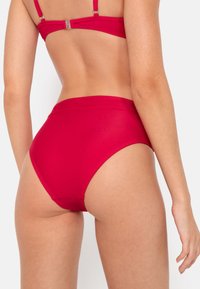 Visoke bikinske hlačke v enotni rdeči barvi z gladkim materialom, minimalnim šivanjem in elegantnim dizajnom, ki vključuje udoben pas.