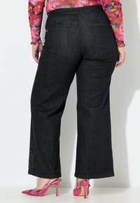 I pantaloni larghi di denim scuro presentano un'alta vita, tasche posteriori e un accento laterale di piccoli borchie. Abbinati a scarpe con tacco rosa.