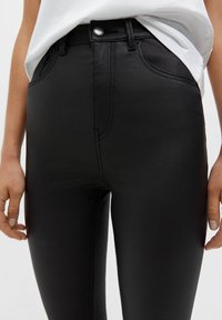 Schwarze Skinny-Jeans aus Kunstleder mit hoher Taille, Knopfverschluss oben und vorderen Taschen. Glatte Textur mit dezenten Nahtdetails.