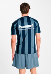 Granatowo-turkusowa sportowa koszulka w paski z napisem "hummel PERFORMANCE" na plecach w białym kolorze, zestawiona z szarymi sportowymi szortami z siateczki.