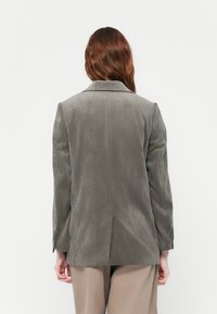 Gray corduroy blazer featuring a notched lapel, long sleeves, and a vent at the back, with a textured vertical stripe pattern.