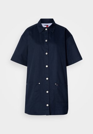 Tamno plava haljina-košulja s kratkim rukavima, izrađena od pamuka. Ima kopčanje na gumbe sprijeda, dva prednja džepa i ovratnik s prugastim unutrašnjim dijelom.