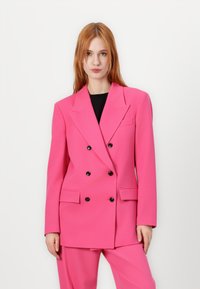 Double-breasted pink blazer in textured fabric, featuring peak lapels, two front pockets, and black buttons, styled with matching pants.